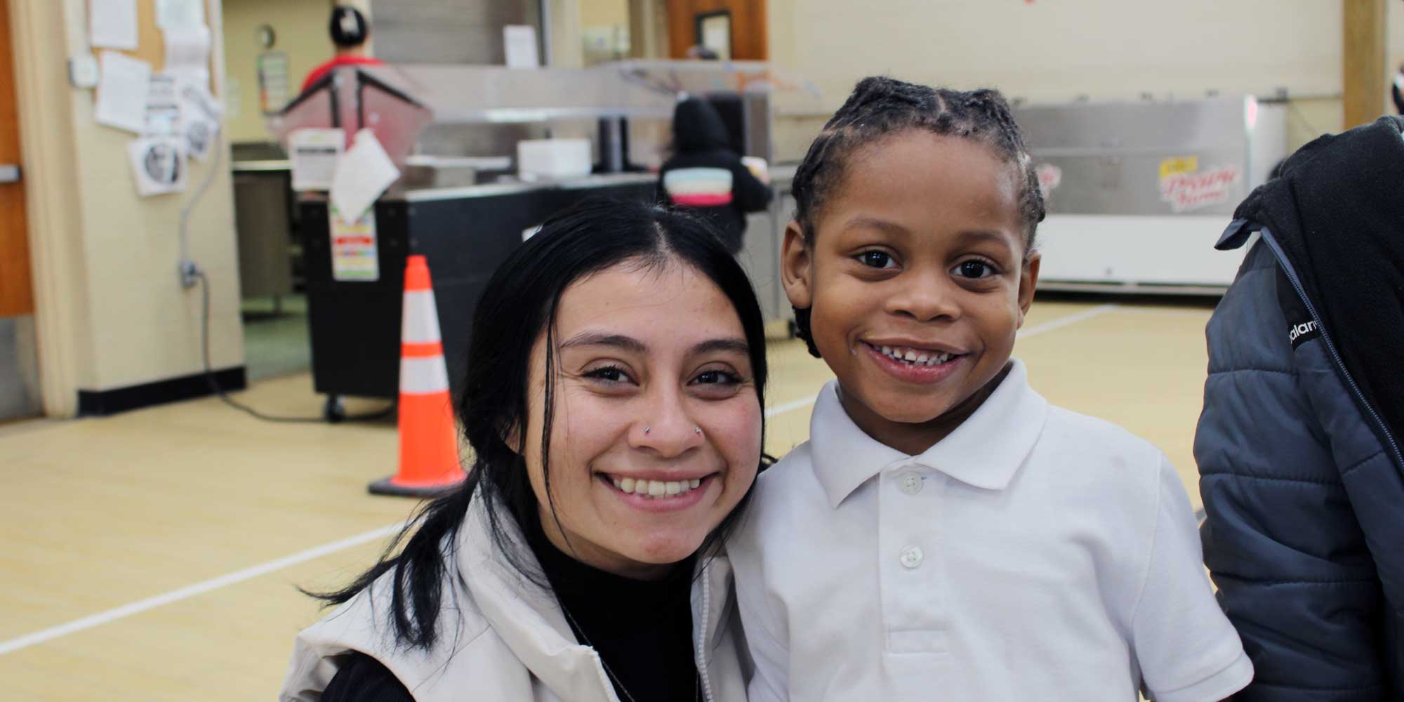 Smiling adult and young student posing together inside the school.